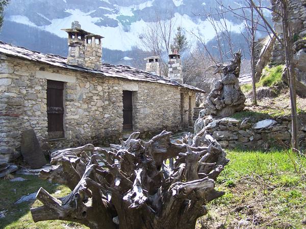Old stone houses with slate roofs, weathered wood stumps and snowy mountains