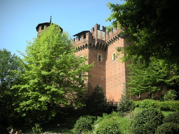 Brick castle with battlements and tower, surrounded by green park trees