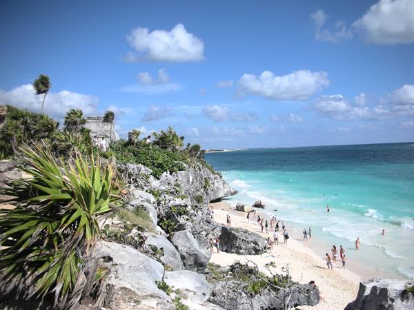 Tourists on the beach below the Mayan ruins of Tulum on limestone cliffs