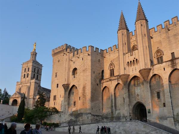 Visitors walk by the stone Popes' Palace of Avignon at dusk
