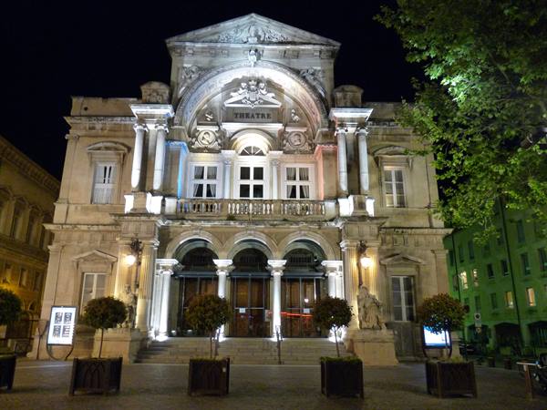 Stone theatre illuminated at night, with arches, columns and statues beside the entrance