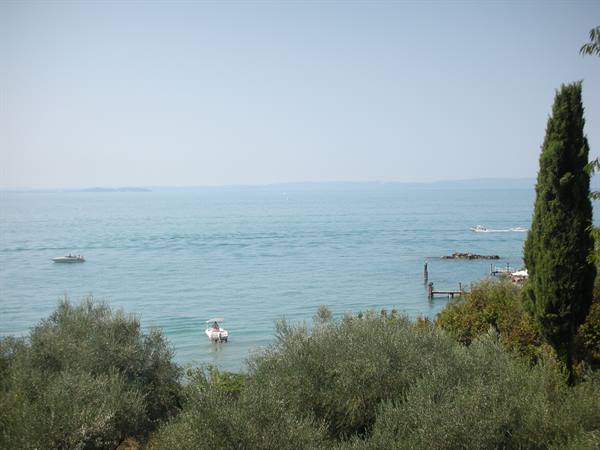 Boats on the blue water of Lake Garda among olive trees and cypress