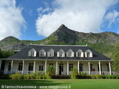 White colonial house with veranda and dormer windows beneath a mountain