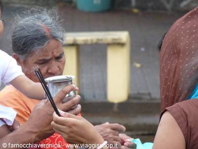 Indian woman in sari receives a drink from a metal cup on the street