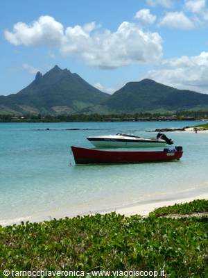Red boat and white motorboat on turquoise water, green mountains behind