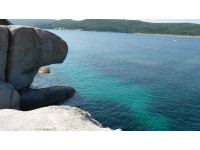 Granite rocks jutting over turquoise water, green hills and a white boat afar