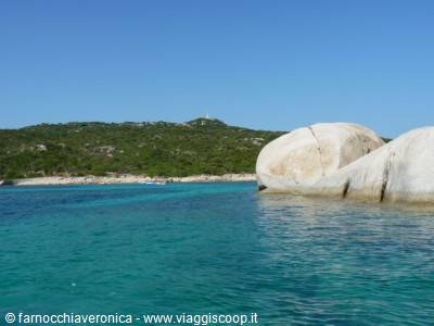 White granite boulders over turquoise water, green Mediterranean scrub behind