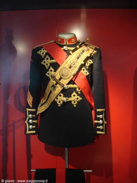 Black military uniform with gold embroidery and red sash on museum display