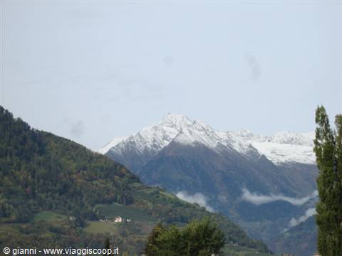 Snow-capped peaks above wooded hills and village, gray sky, low clouds