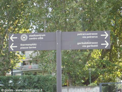 Bilingual German-Italian street signpost pointing to city center and thermal baths, Merano