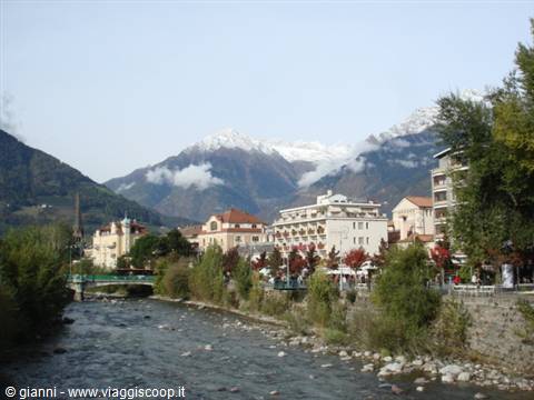 The Passer river flows through Merano with pastel buildings and snowy mountains