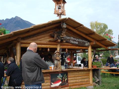 Wooden log kiosk with bell and carved sign, people at counter, mountains behind