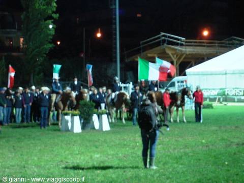 Photographer films riders with Italian flags at a night award ceremony on grass