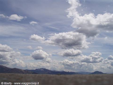 White clouds over dark distant mountains, arid ground in foreground