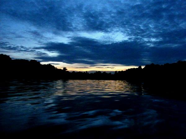 Dark clouds over rippled water, tree silhouettes at dusk