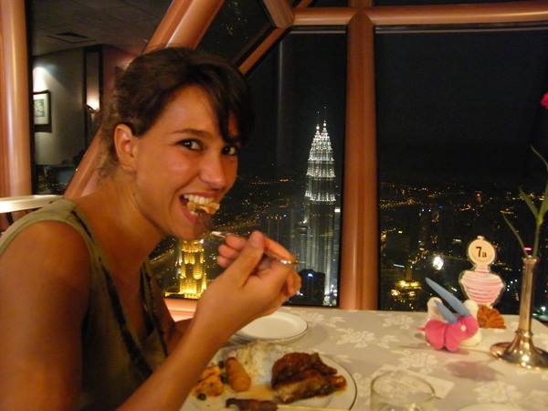 Woman eating at restaurant with illuminated Petronas Towers behind