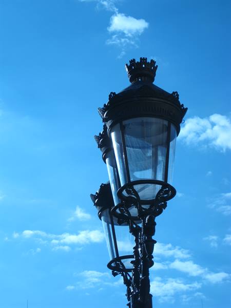 Ornate wrought-iron street lamp with crown against blue sky