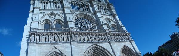 Gothic facade of Notre-Dame in Paris, rose window and stone statues under blue sky