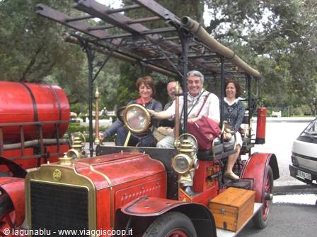 Smiling tourists riding an old red vintage car with brass headlamps