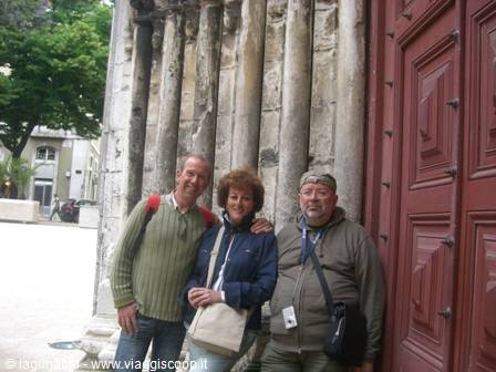 Three friends posing by weathered stone columns and a carved red door