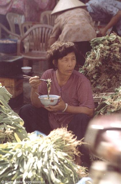 Woman eating noodles with chopsticks at a vegetable market