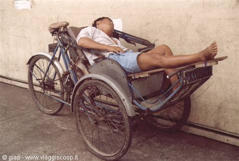 Cyclist sleeping on a pedal rickshaw beside a white wall