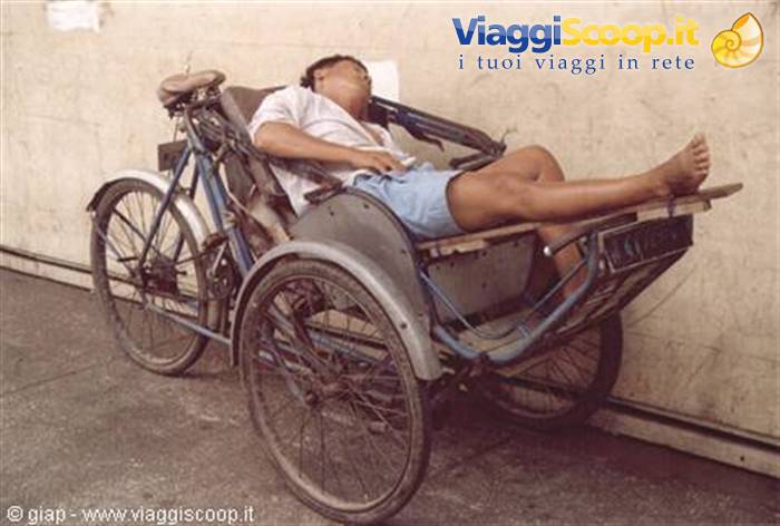 Cyclist sleeping on a pedal rickshaw beside a white wall