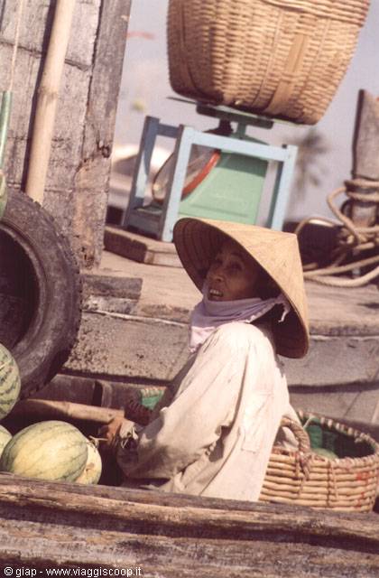 Woman in straw hat selling watermelons from a wooden boat