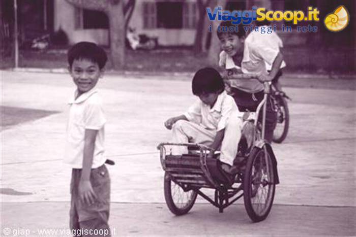 Smiling children in a courtyard, one riding a pedal rickshaw