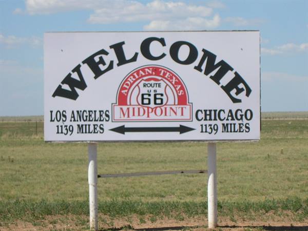 White Midpoint Route 66 sign in Adrian, grassland and blue sky