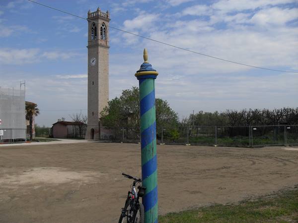 Bike leaning on a blue and green striped pole, clock bell tower behind