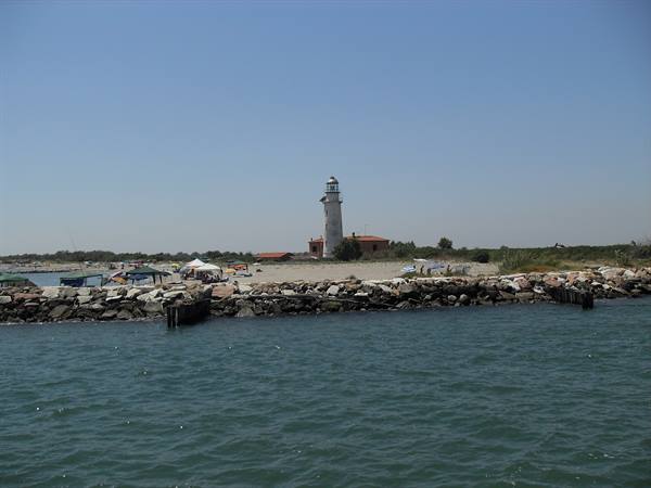 Bibione lighthouse behind the rocky breakwater, blue sea in the foreground