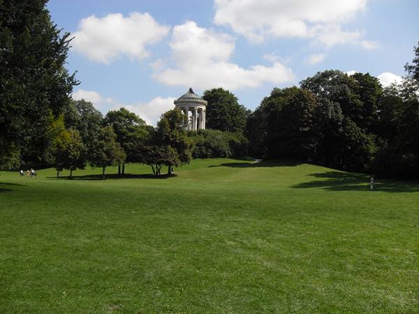 The Monopteros above the green lawn of the Englischer Garten, people strolling among trees