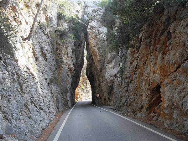 Asphalt road between rock walls with natural stone arch