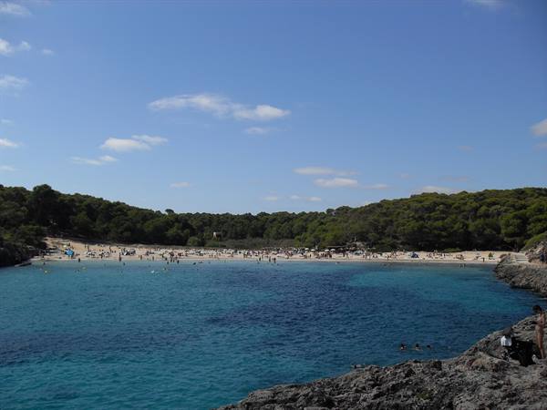 Bathers on sand and turquoise water among rocks and pines