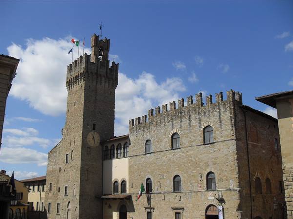 Crenellated stone tower with flags and clock, medieval palace in Arezzo