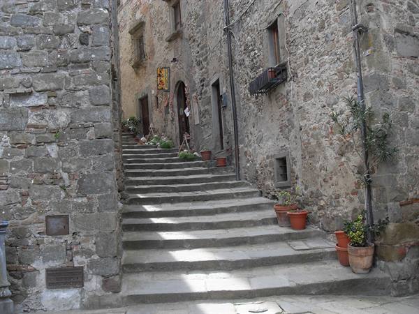 Stone stairway between medieval houses with terracotta pots, sunlight