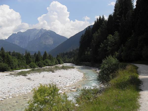 Mountain river over gravel bars, conifer forest and dolomite peaks under clouds