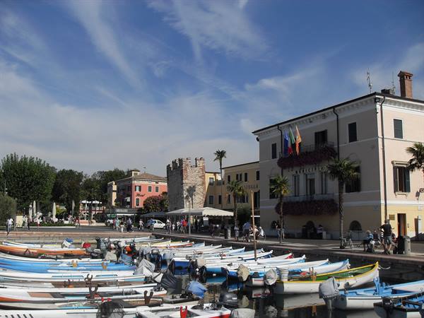 Colorful boats moored at Bardolino harbor, pastel buildings and medieval tower