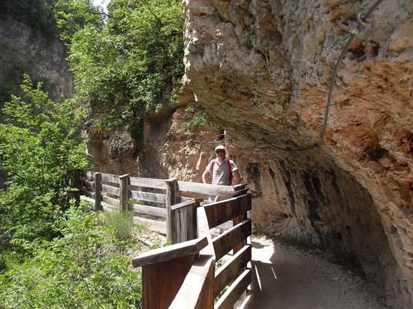 Hiker walking a dirt path with wooden railings carved into the rock