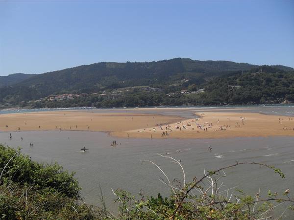 Bathers on exposed sand at low tide, green hills behind
