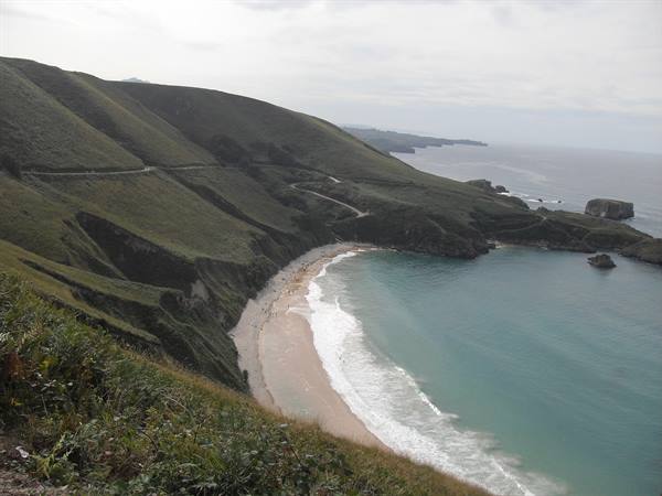 Torimbia beach, pale sand between green hills and cliffs under grey sky