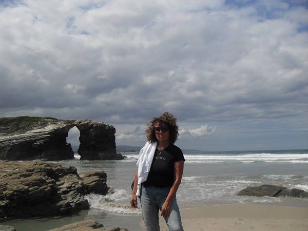 Woman in black shirt on rocky beach in front of natural sea arch, As Catedrais beach