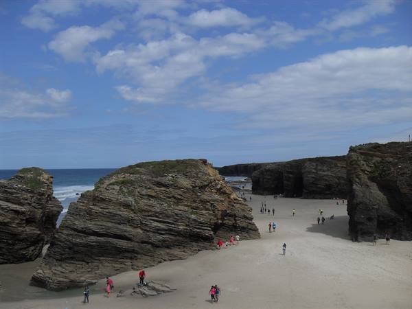 Tourists walking on sand between rounded rock formations, Playa de las Catedrales