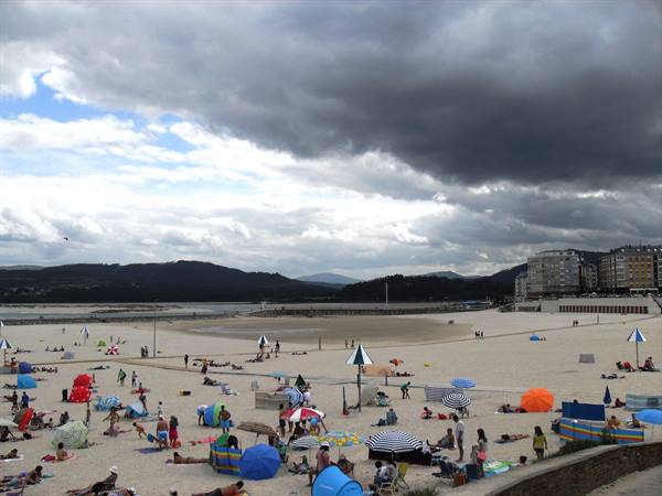 Urban beach with colorful umbrellas under stormy sky, buildings and mountains behind