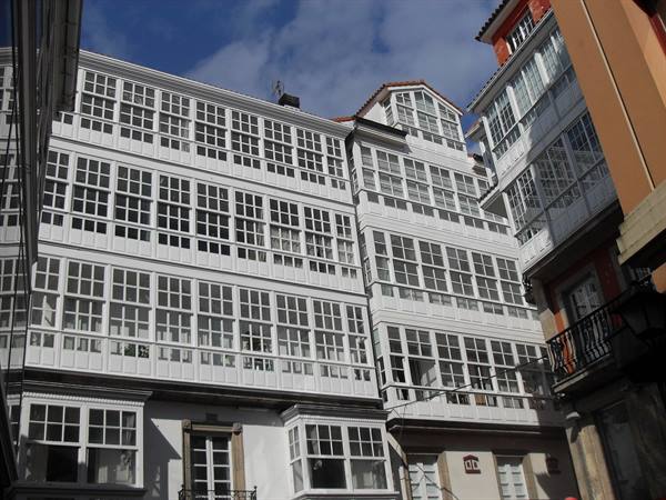 White facade with large glazed balconies on a narrow street in A Coruña