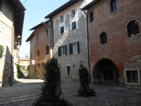 Cobbled square with stone and brick houses, arches and flowering shrubs