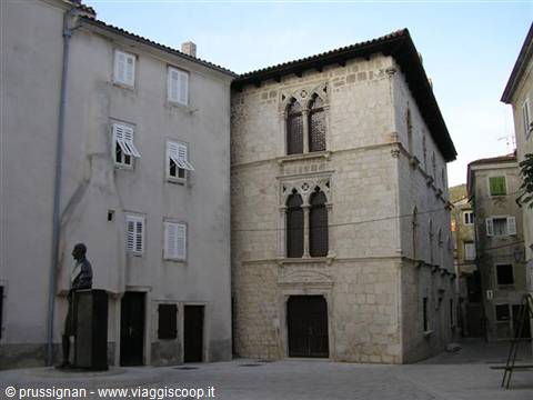 Bronze statue facing a stone palace with Gothic windows