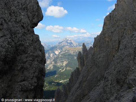 Rocky Dolomite walls frame jagged peaks and forested valley beneath white clouds