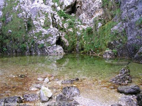 Clear green pool among limestone rocks and moss, pebbles on the bottom